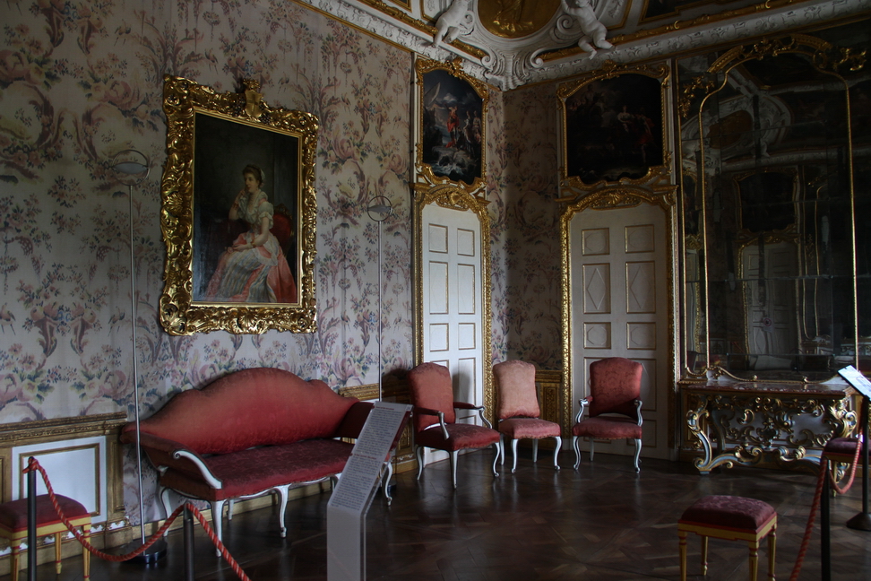 Villa della Regina_033.JPG - Appartamento del Re "Camera del letto verso ponente".la stanza è il risultato di successivi interventi decorativi. Il primo fu affidato a Filippo Juvarra dalla Regina Anna Maria d'Orléans e vide, tra il 1718 e il 1720, la realizzazione della volta con stucchi e dipinti di Claudio Francesco Beaumont raffiguranti le Stagioni e il Carro di Apollo.Un secondo invece, da situare a partire dal 1730, va riferito alla committenza di Carlo Emanuele III e Polissena d'Assia e vide il coinvolgimento di Baroni di Tavigliano.Boiserie e specchiere erano completate da tappezzeria e letto in taffetas "alla china" e da tele con Storie di Enea di Corrado Giaquinto.La tappezzeria, ricollocata ai lati della specchiera, è evocata in copia fotografica su tessuto ignifugo sulle restanti pareti.Dal 1868, dopo il distacco e il trasporto delle sei sovrapporte di Giaquinto al Quirinale - sostituite oggi da copie fotografiche - la sala prese il nome dai ritratti dei sovrani Umberto I e Margherita, qui raffiguratada Luigi Biagi nel 1879.